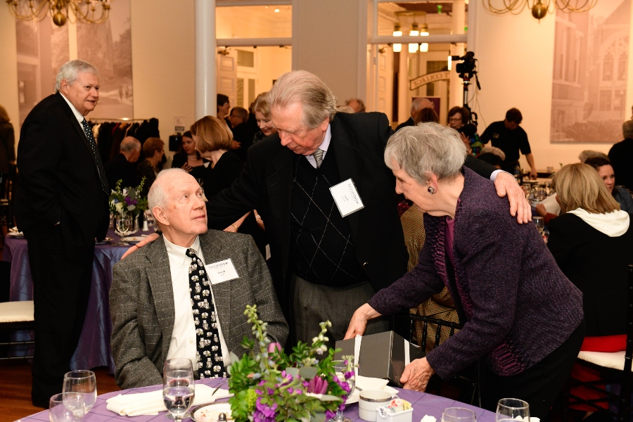 三个人坐在一张铺着紫色桌布的桌子旁互相欢迎.